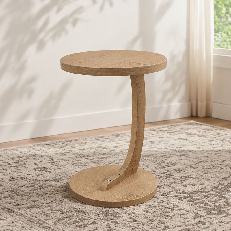 Light brown round end table with pedestal base and lower shelf on carpet