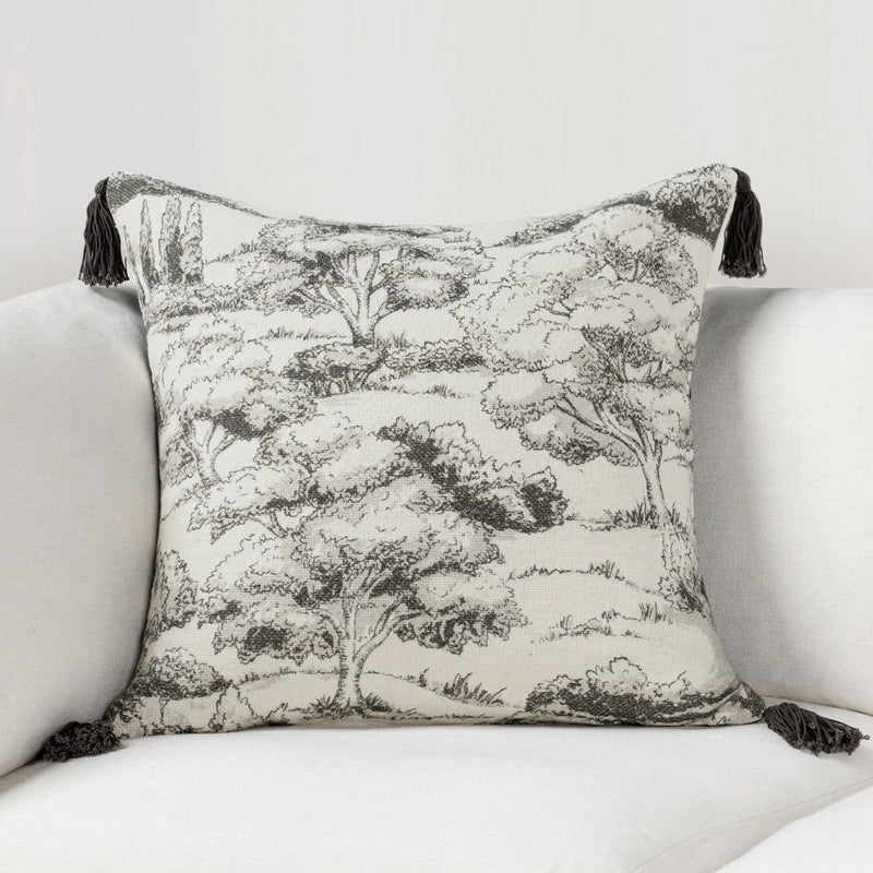 Charcoal forest-print throw pillow with tassels on a sofa, light gray tree pattern.