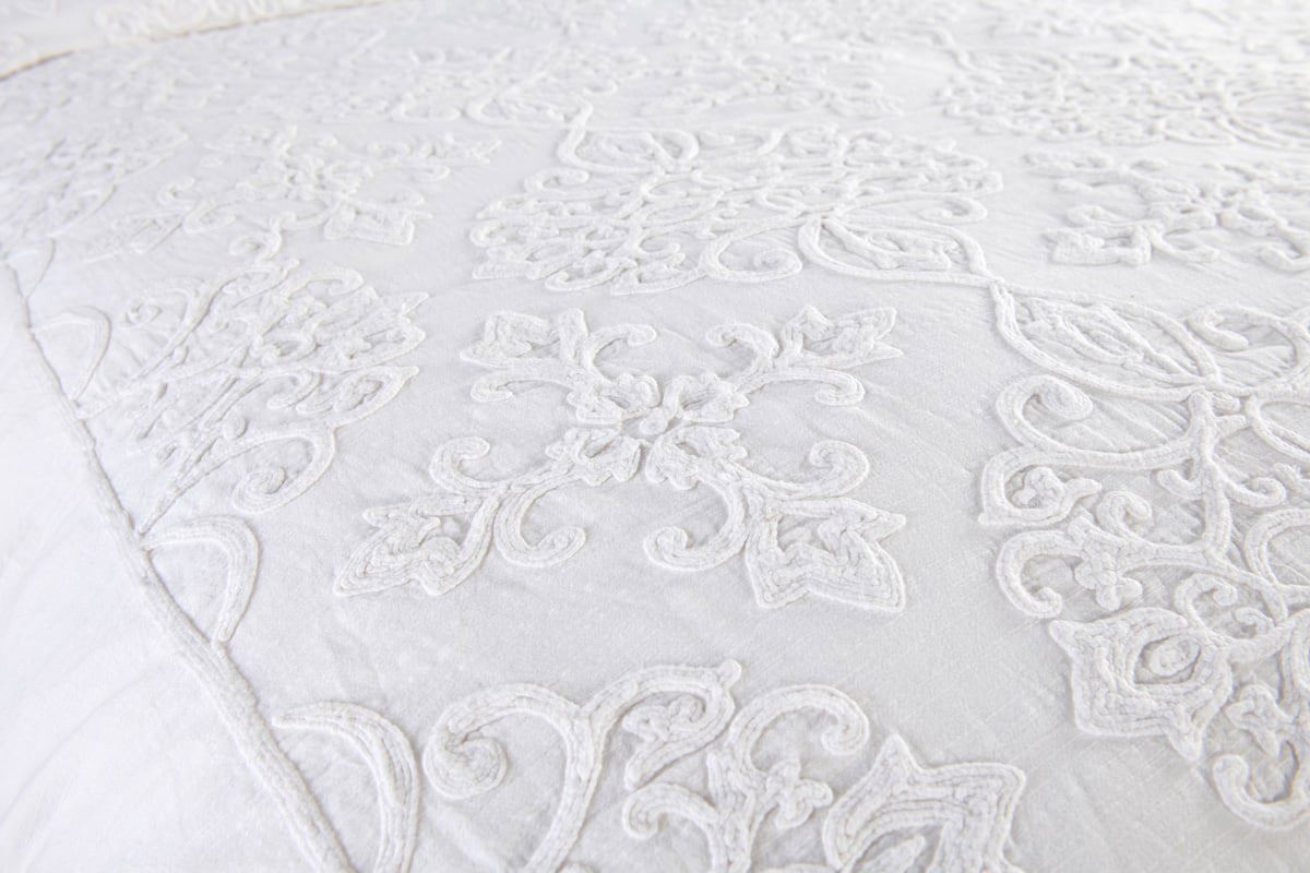 Close-up view of white quilted duvet with intricate scroll embroidery and texture