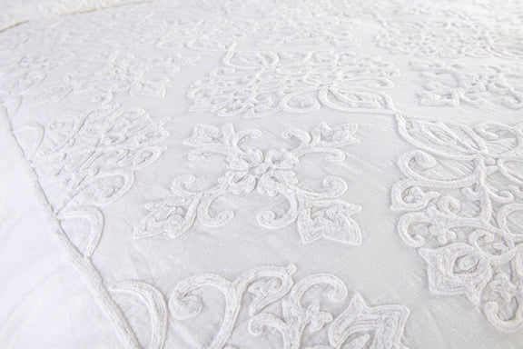 Close-up view of white quilted duvet with intricate scroll embroidery and texture