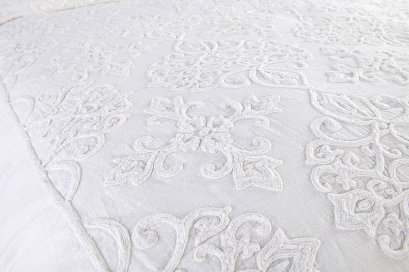 Close-up view of white quilted duvet with intricate scroll embroidery and texture