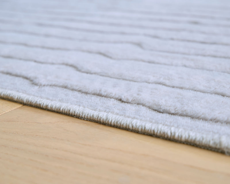 Light gray washable rug with low-pile striped texture and overlock edge