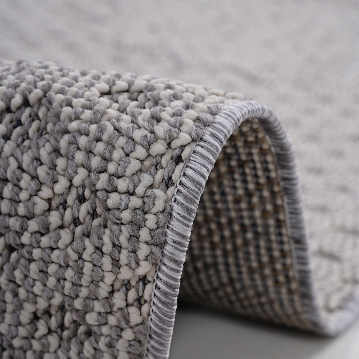 Medallion indoor/outdoor area rug close-up of loop texture and gray bound edge near rolled corner