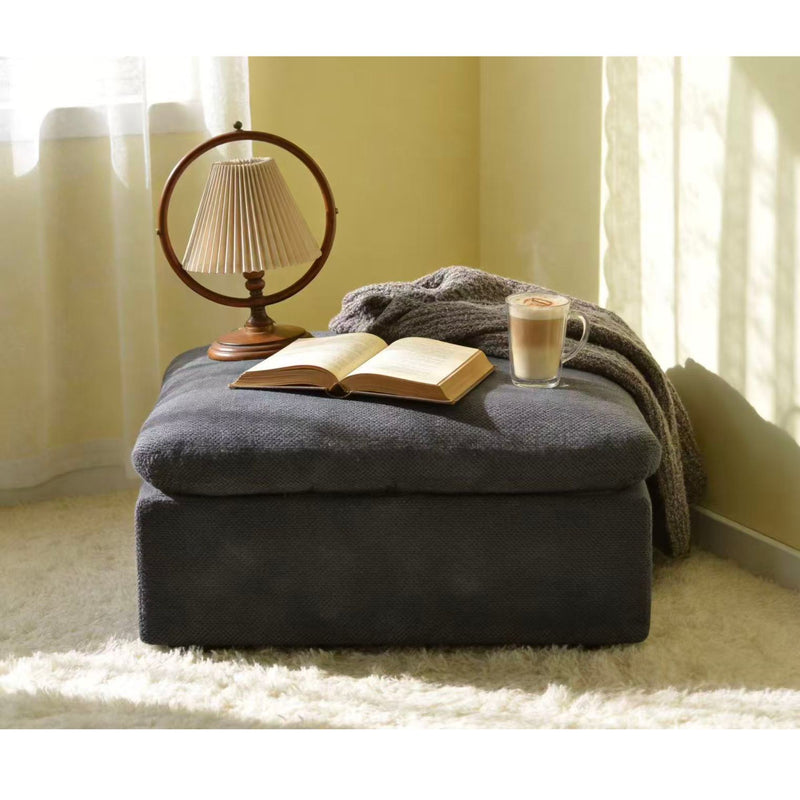 Dark gray upholstered ottoman with low profile and rectangular, padded silhouette