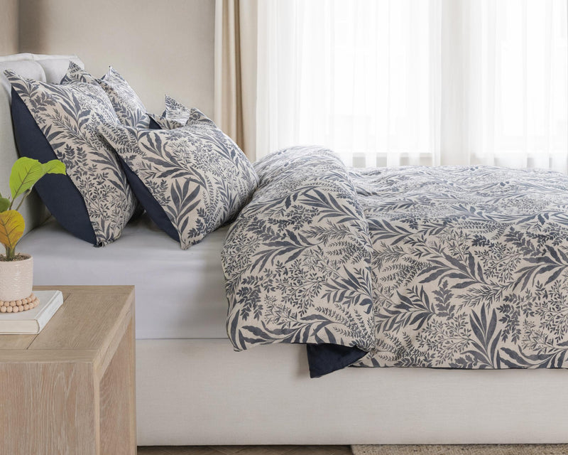 Denim blue leaf-pattern duvet set with layered pillow shams on a bed