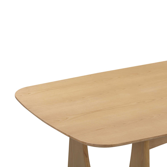 Light brown dining table corner with rounded edge and visible wood grain