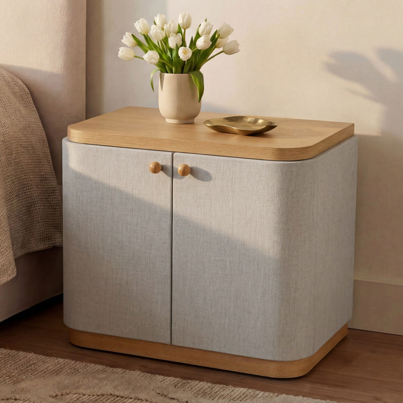 Cream fabric nightstand with wood top, two doors and brass knobs; flowers on top