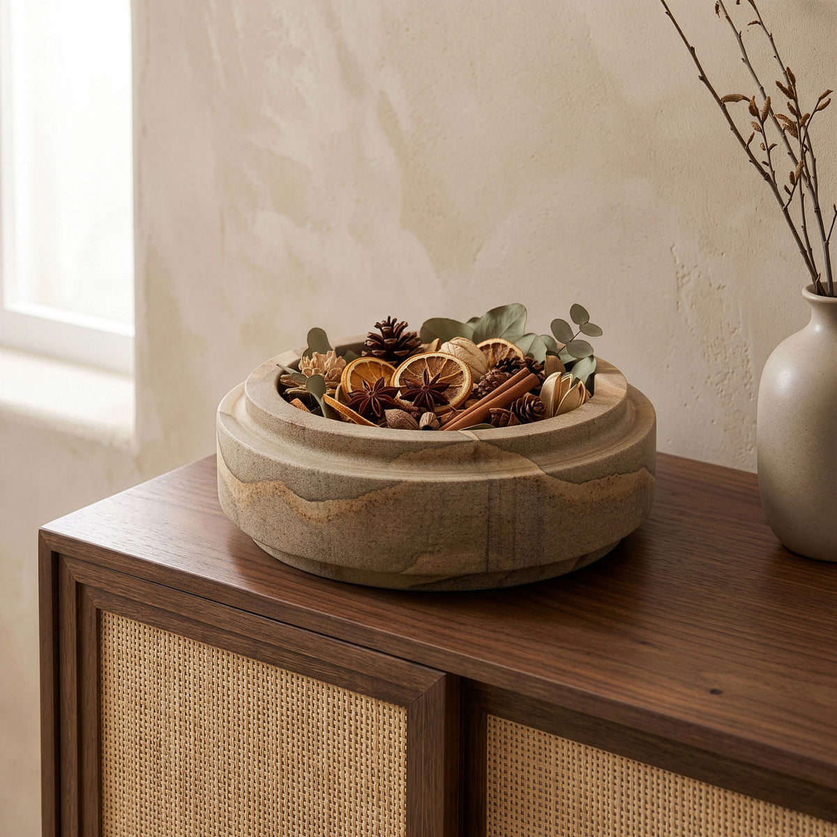 Light brown sandstone bowl on wooden surface filled with dried stems and pods.