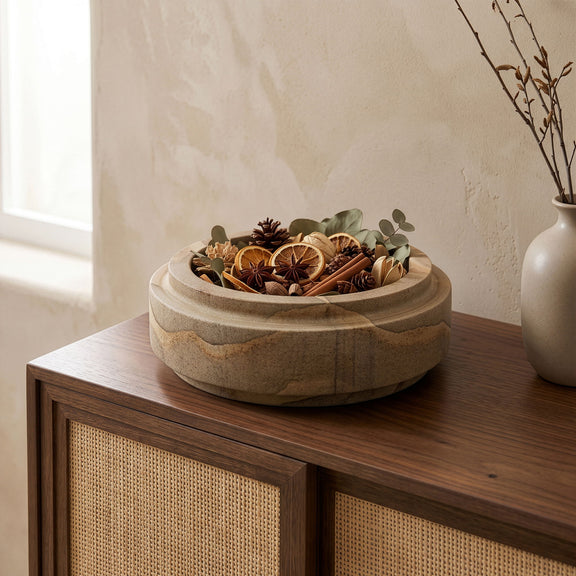 Light brown sandstone bowl on wooden surface filled with dried stems and pods.
