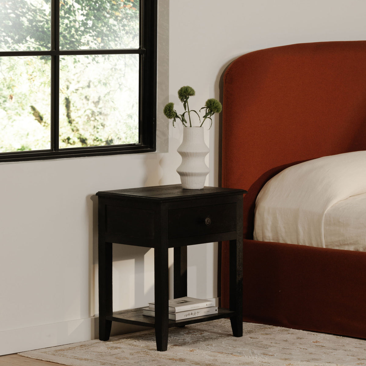 Black nightstand with one drawer and lower shelf near the bed
