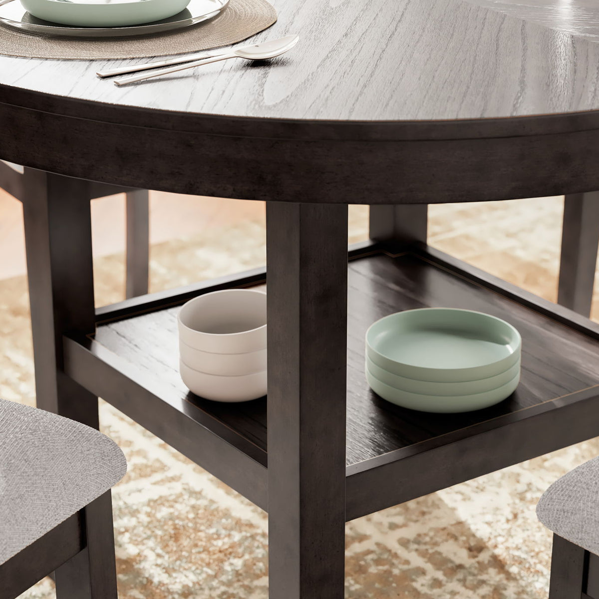 Brown dining table with open shelf and gray upholstered chair corner view
