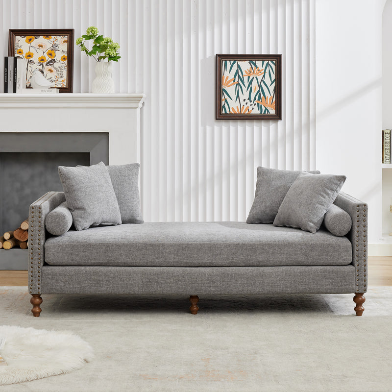 Gray upholstered chaise lounge with nailhead trim and two throw pillows