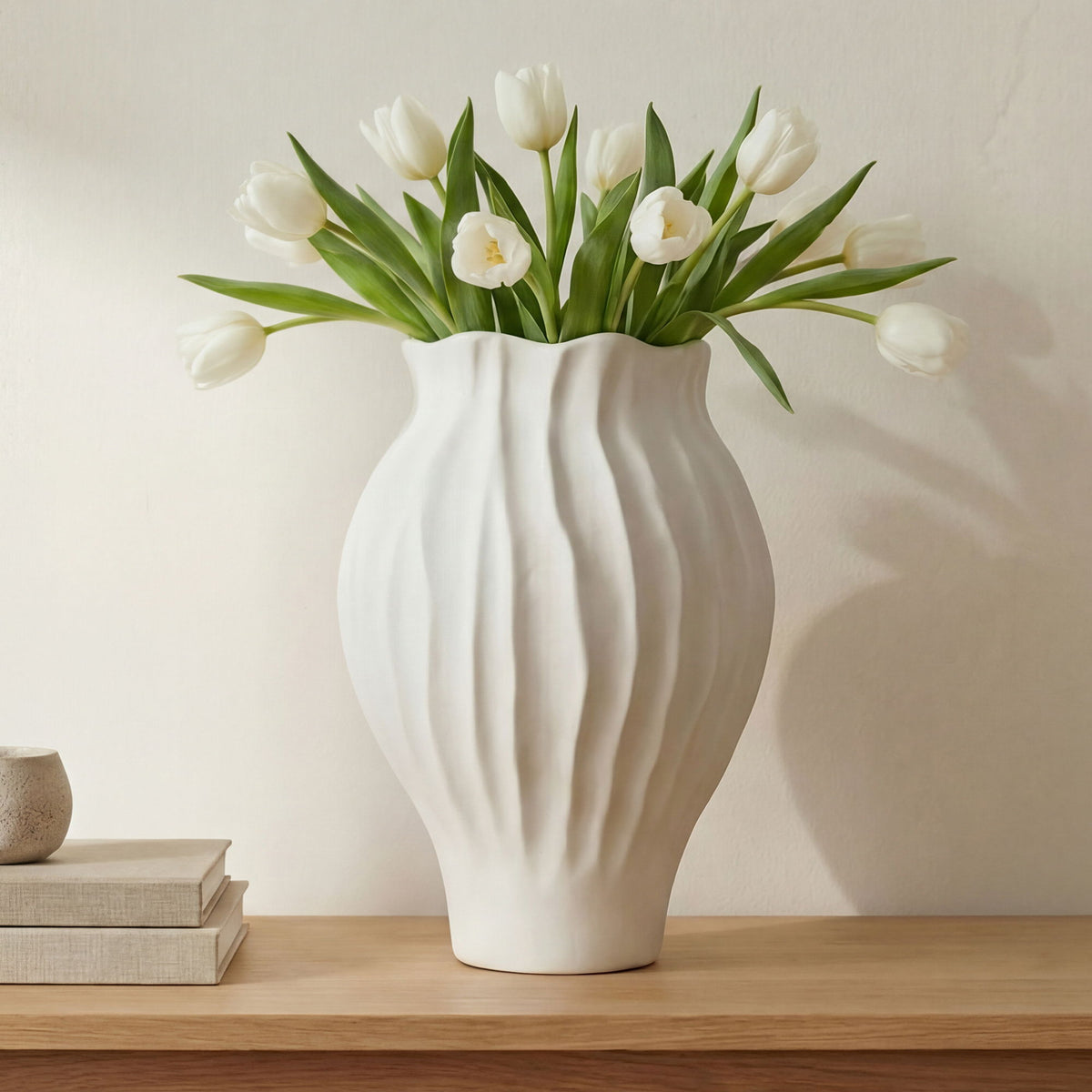 White ribbed ceramic vase holding white tulips with green leaves