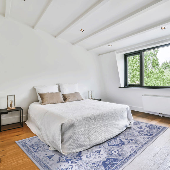 Blue and white patterned area rug beneath a bed in a bright room