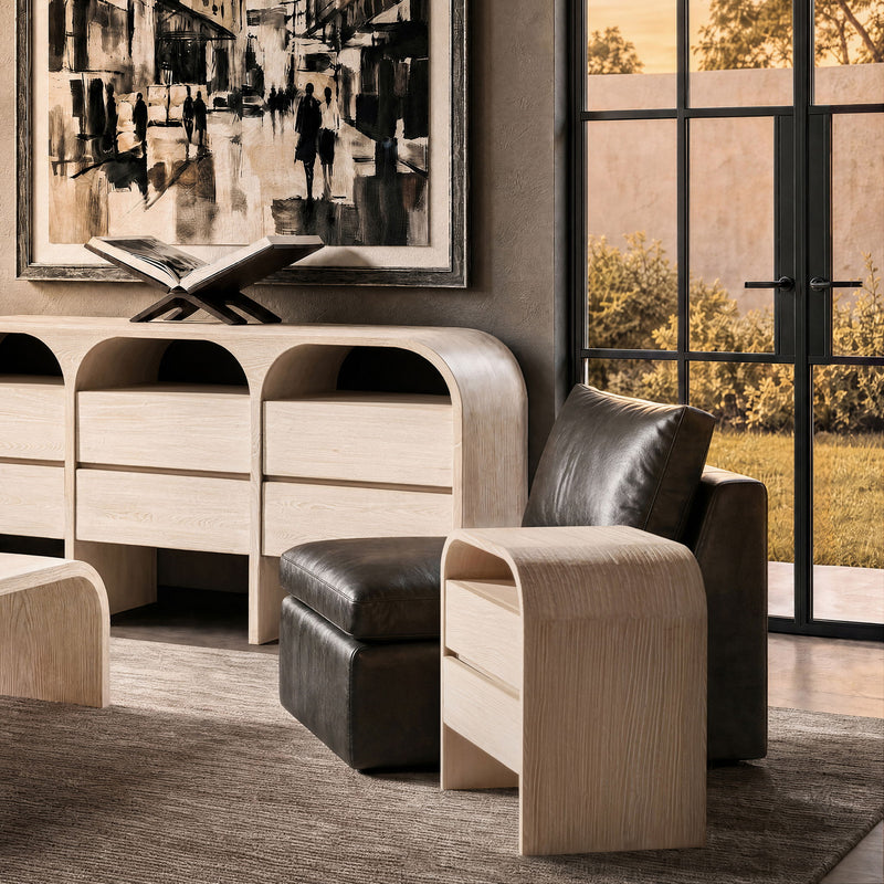 White-washed side table with curved sides and two drawers beside an armchair