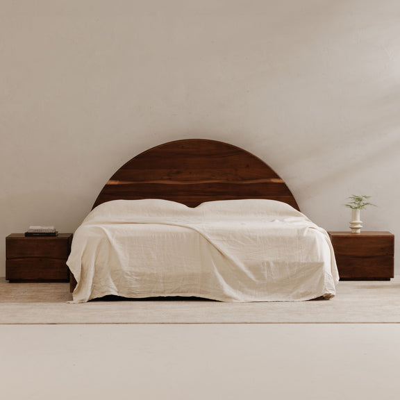Brown wooden king bed with arched headboard and white bedding draped over mattress