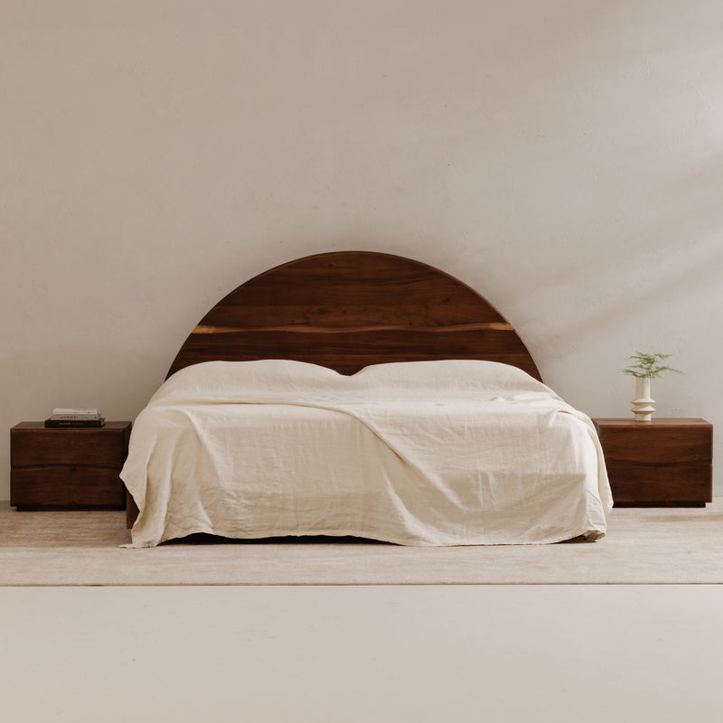 Brown wooden king bed with arched headboard and white bedding draped over mattress