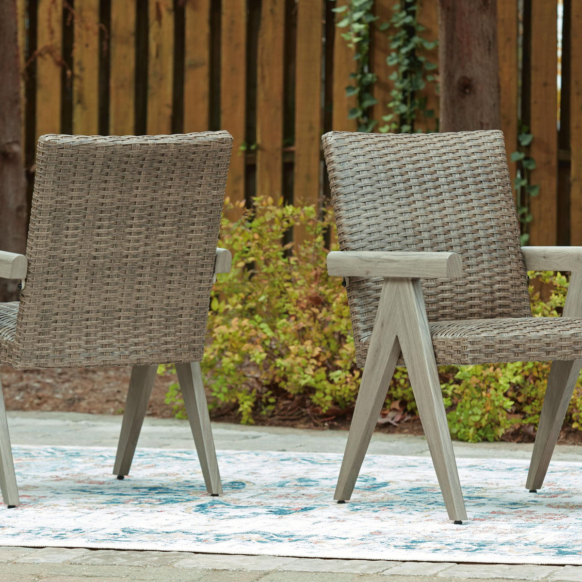 Outdoor beige woven armchairs with light wood arms, matching seat and back