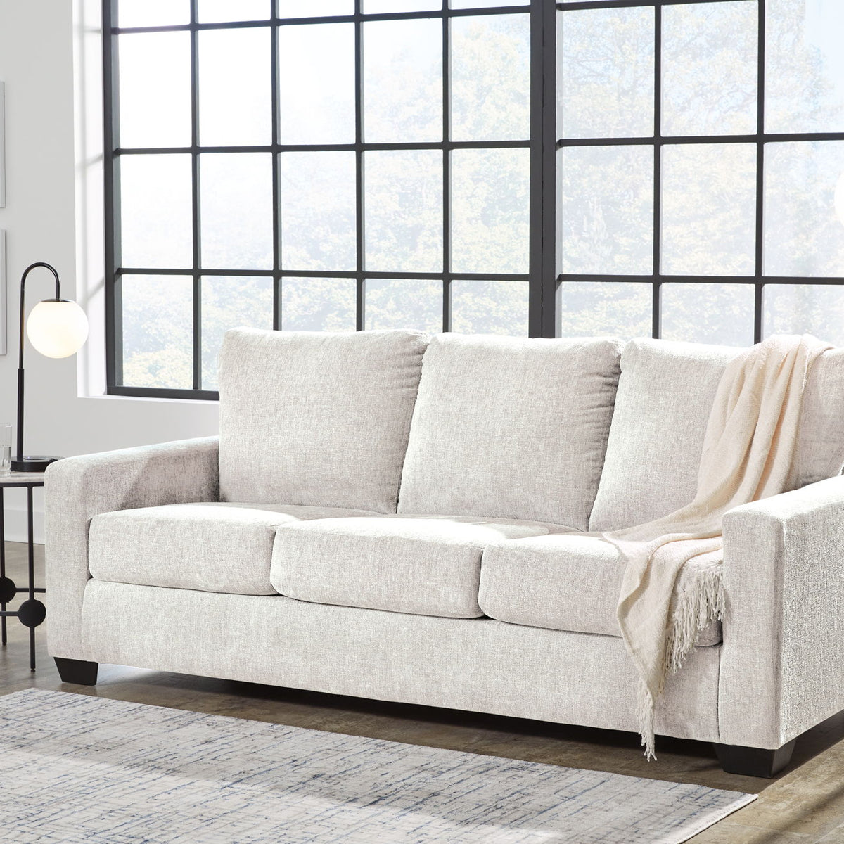 Beige 3-seat sofa with three back cushions and armrests, with a light throw blanket