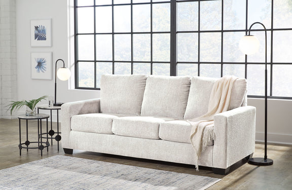 Beige 3-seat sofa with three back cushions and armrests, with a light throw blanket
