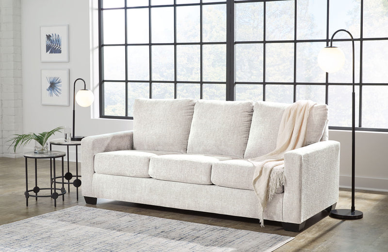 Beige 3-seat sofa with three back cushions and armrests, with a light throw blanket