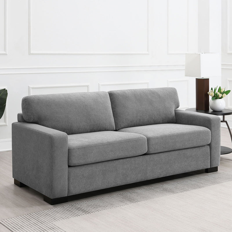 Gray fabric sleeper sofa with plush back cushions, rolled arms, and black feet
