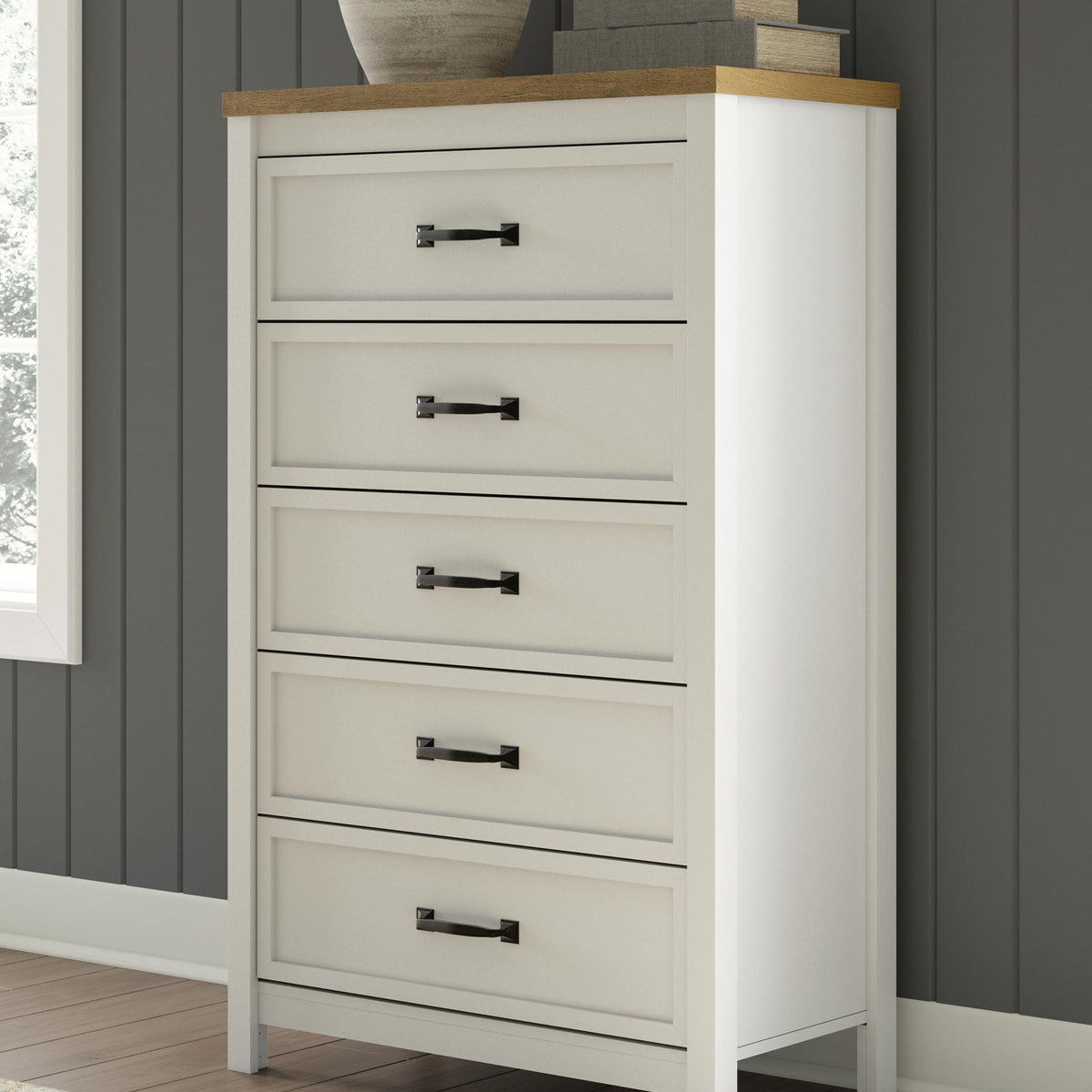 White five-drawer chest with brown top and black bar handles, in-room angled view