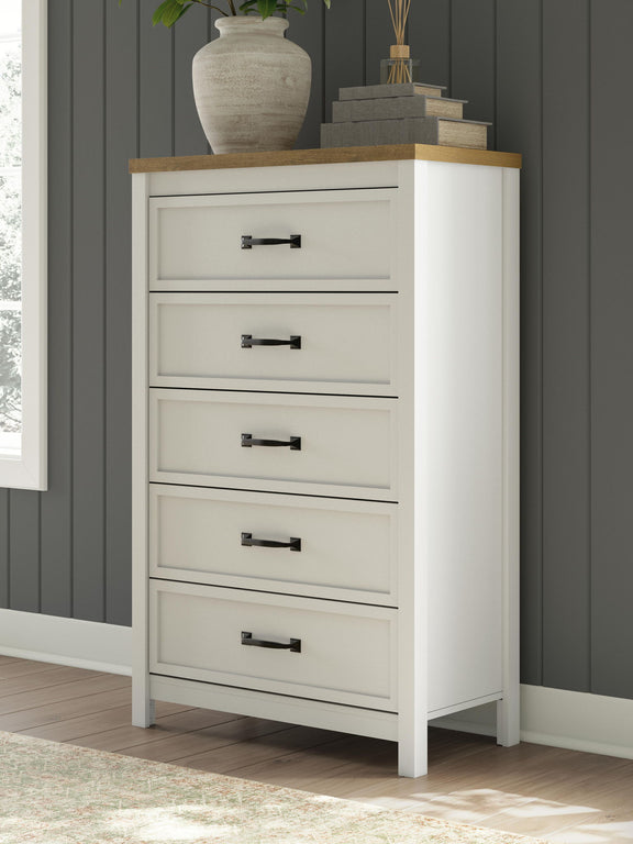 White five-drawer chest with brown top and black bar handles, in-room angled view