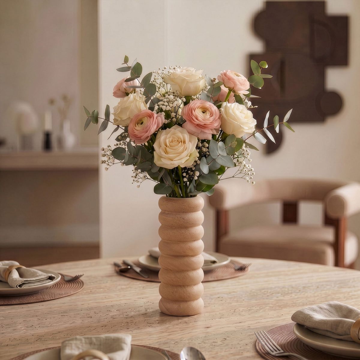 Sandstone vase with ribbed stem base holding a floral bouquet on a table