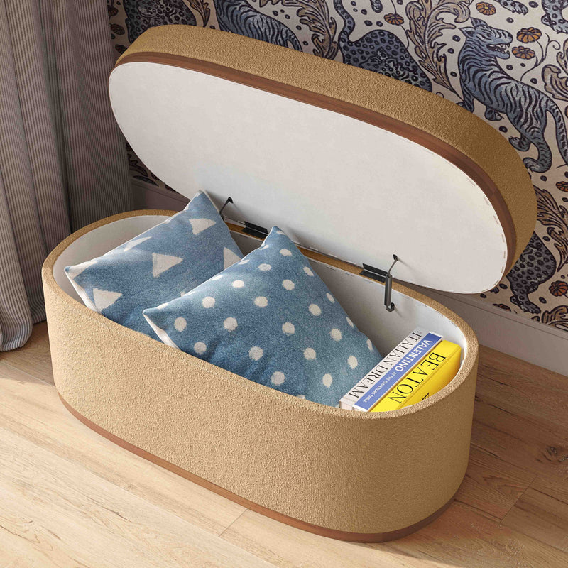Beige boucle oval storage ottoman with open lid, holding blue polka-dot fabric and books