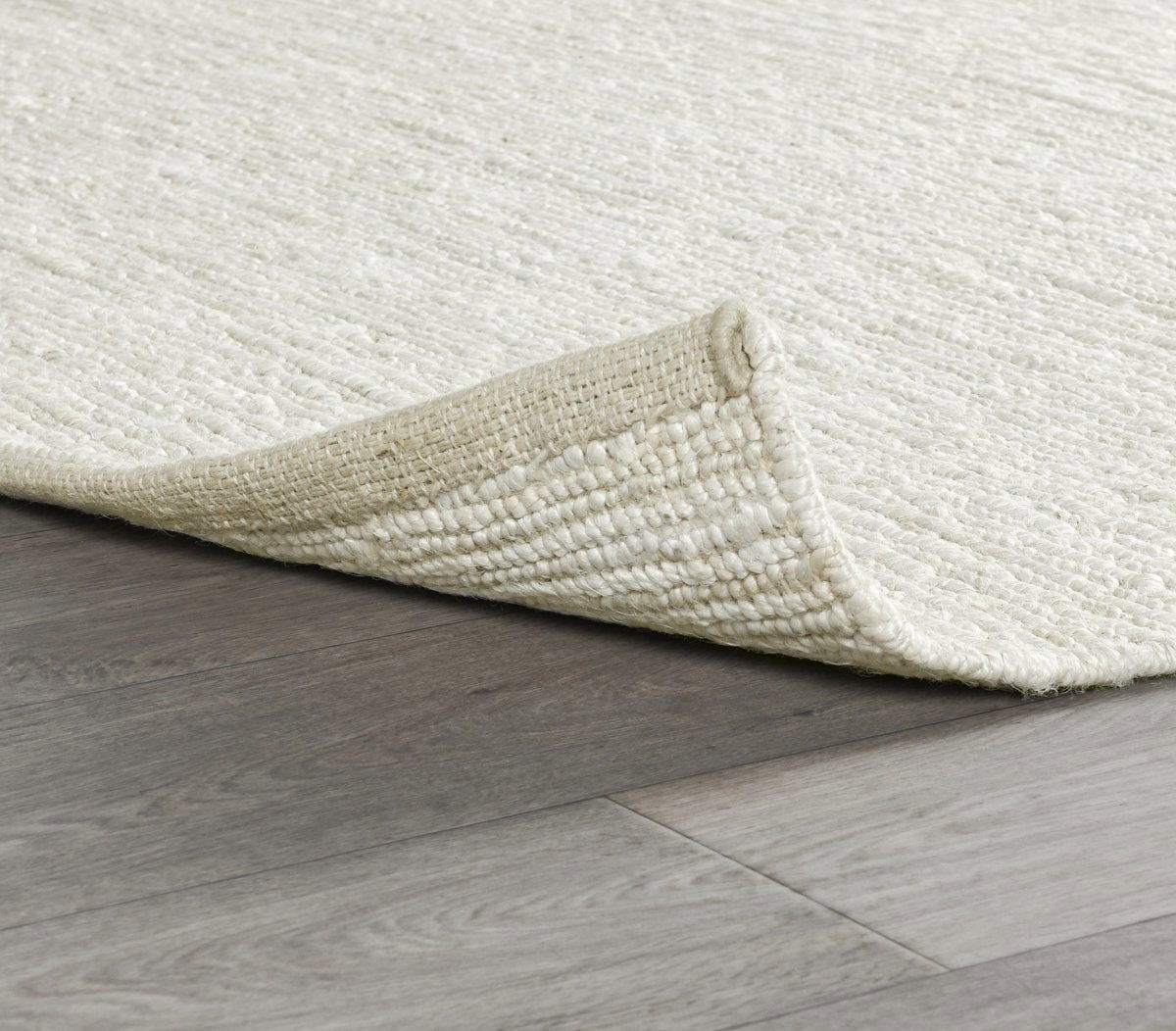 Ivory white jute rug corner on hardwood, flatwoven weave and textured pile.