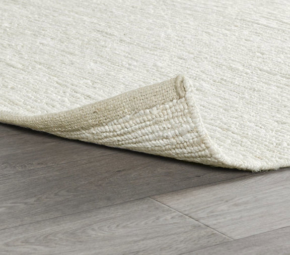 Ivory white jute rug corner on hardwood, flatwoven weave and textured pile.