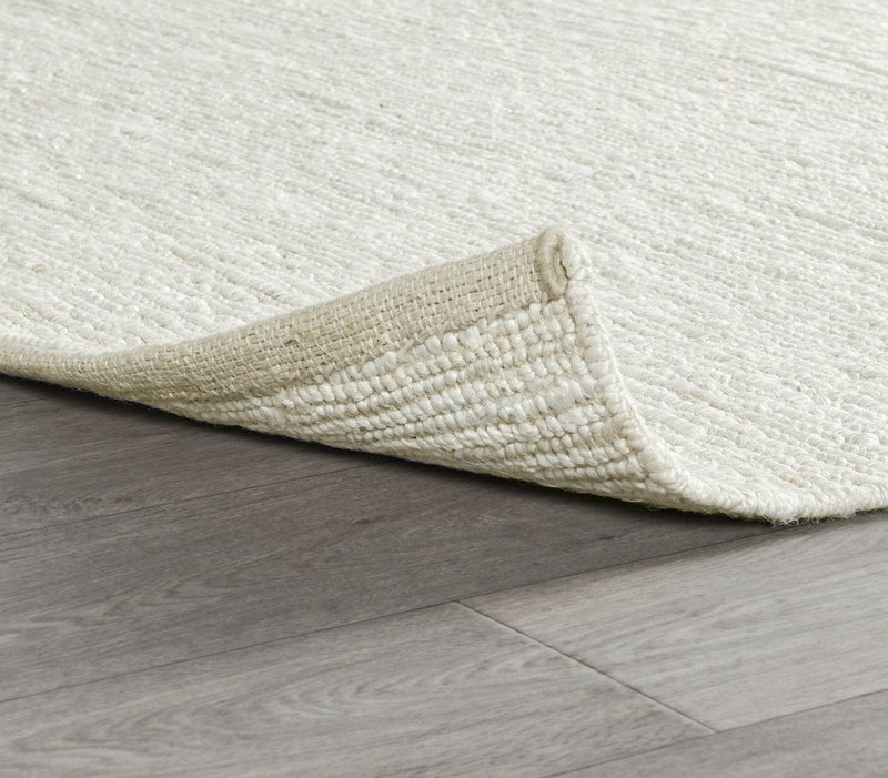 Ivory white jute rug corner on hardwood, flatwoven weave and textured pile.