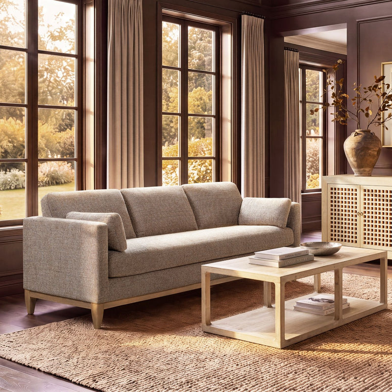 Light beige upholstered sofa with three back cushions, boxy arms, and tapered wood legs
