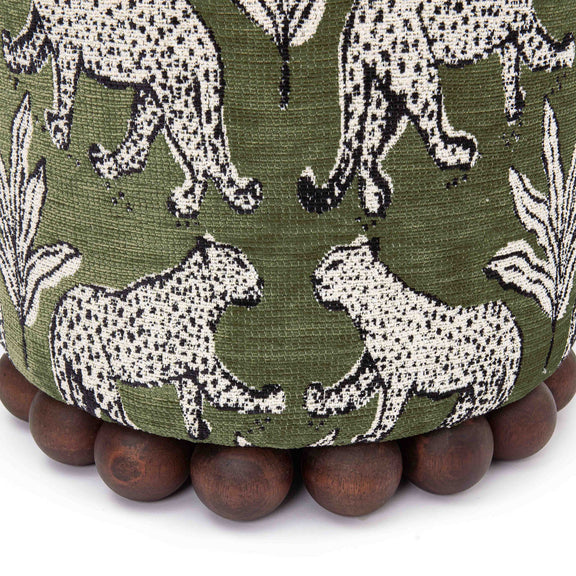 Close-up of dark green ottoman fabric with white animal pattern and dark wood ball base.