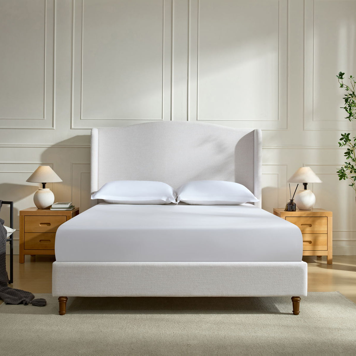 Beige upholstered wingback bed with tall headboard, pillows, and wooden legs