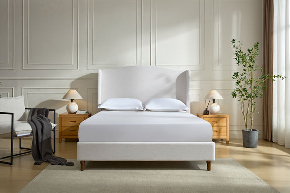 Beige upholstered wingback bed with tall headboard, pillows, and wooden legs