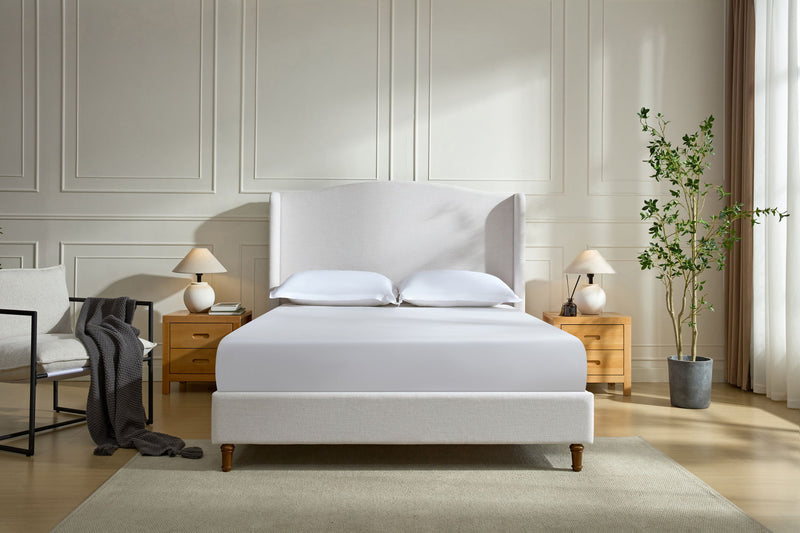 Beige upholstered wingback bed with tall headboard, pillows, and wooden legs