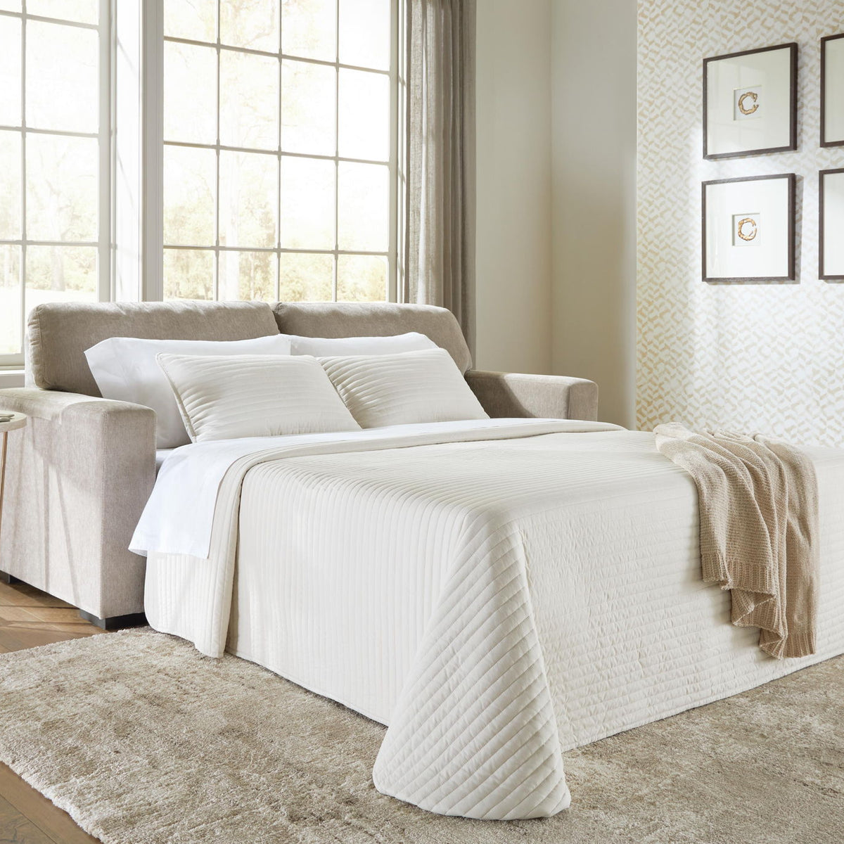 Beige sofa sleeper opened into a bed with white bedding and throw blanket